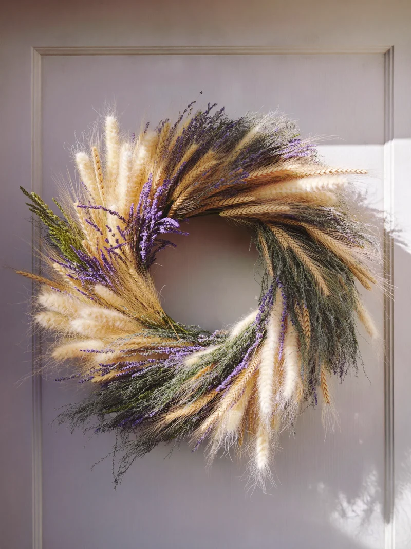Couronne artificielle de blé, lavande et herbes blanchies accrochée à une porte en bois peint