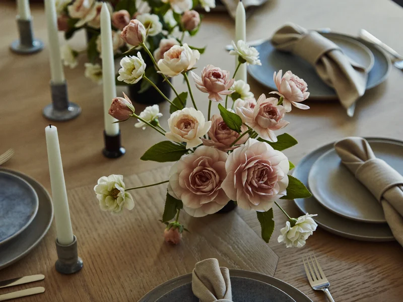 Table dressée avec un centre de table floral artificiel bas, lin, grès et bougies